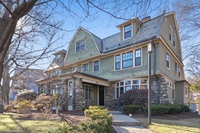 view of front facade with stone siding, a chimney, and a gambrel roof