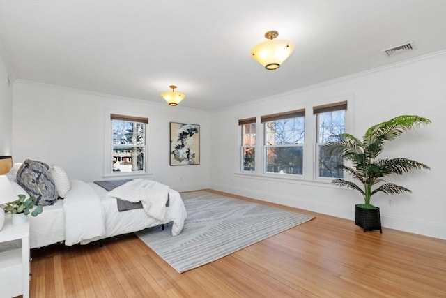 bedroom featuring visible vents, crown molding, baseboards, and wood finished floors