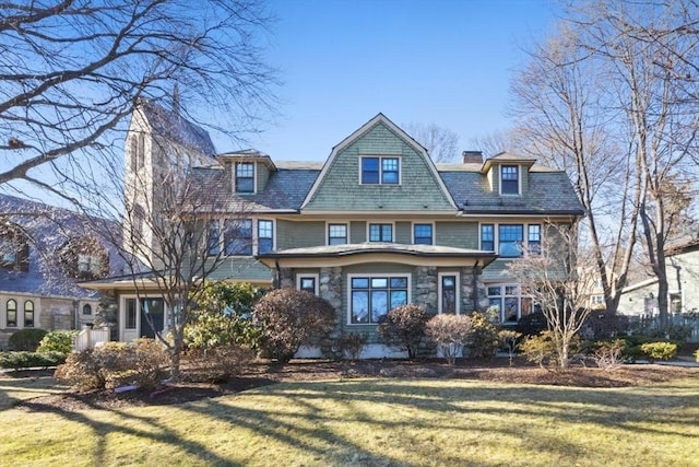 view of front facade featuring a gambrel roof, stone siding, a chimney, and a front lawn