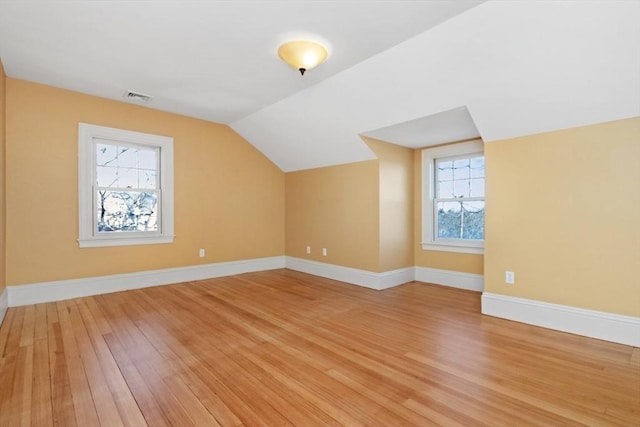 additional living space featuring vaulted ceiling, light wood-type flooring, visible vents, and baseboards