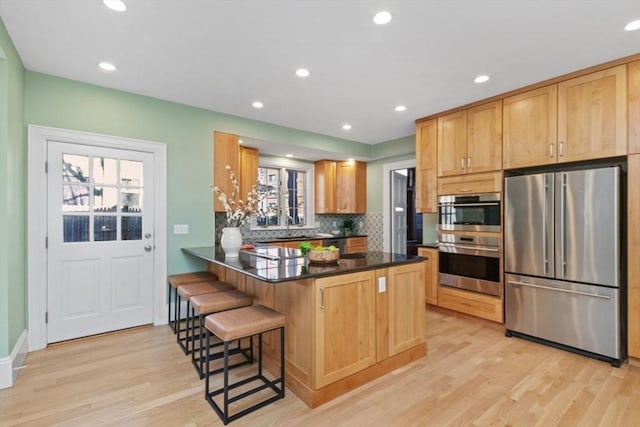 kitchen with light wood-style flooring, stainless steel appliances, a kitchen breakfast bar, decorative backsplash, and dark countertops