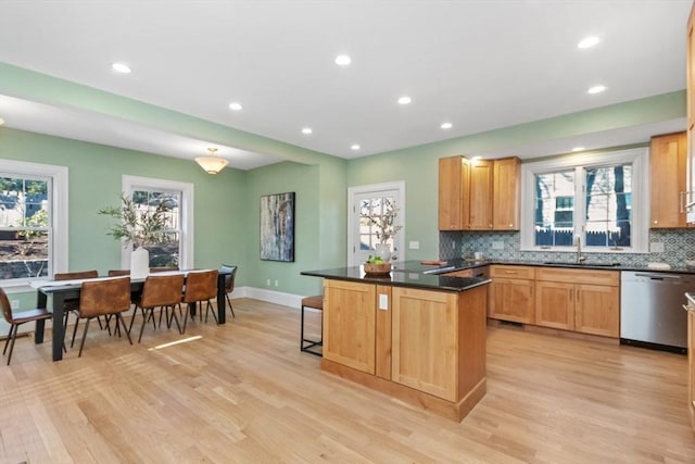 kitchen featuring a sink, light wood-style floors, dishwasher, tasteful backsplash, and dark countertops