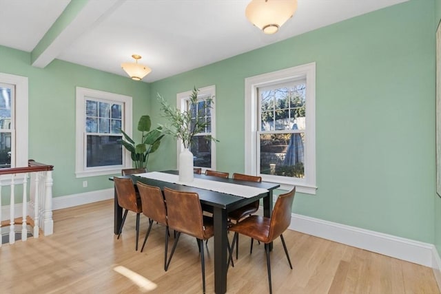 dining area featuring beam ceiling, light wood finished floors, and baseboards