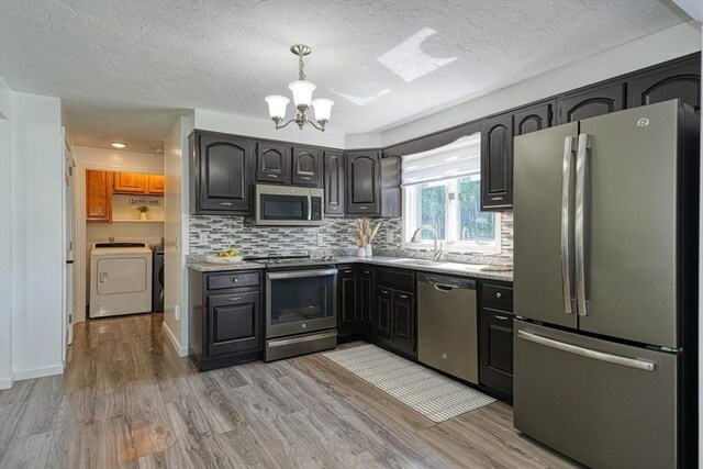 13 Woodland Dr, Hudson, MA 01749 - kitchen with appliances with stainless steel finishes, washer and dryer, a chandelier, light wood finished floors, and backsplash