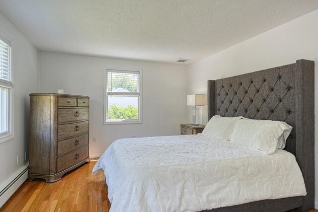 13 Woodland Dr, Hudson, MA 01749 - bedroom with a baseboard heating unit, light wood-style flooring, and a textured ceiling