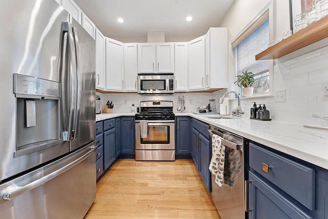 kitchen featuring white cabinets, backsplash, stainless steel appliances, blue cabinetry, and light hardwood / wood-style flooring