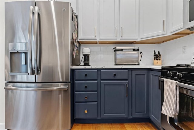 kitchen with white cabinets, tasteful backsplash, stainless steel fridge, and gas range oven