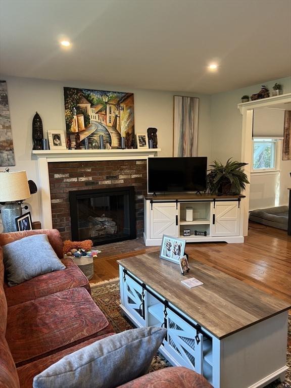 living room with recessed lighting, a brick fireplace, and wood finished floors