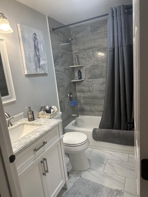full bathroom with shower / bath combo with shower curtain, toilet, marble finish floor, and vanity