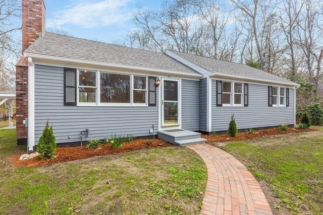 view of front of house with a shingled roof, a front lawn, and a chimney