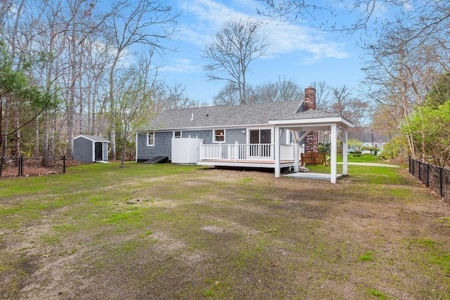 back of property featuring fence, roof with shingles, a wooden deck, a chimney, and a yard