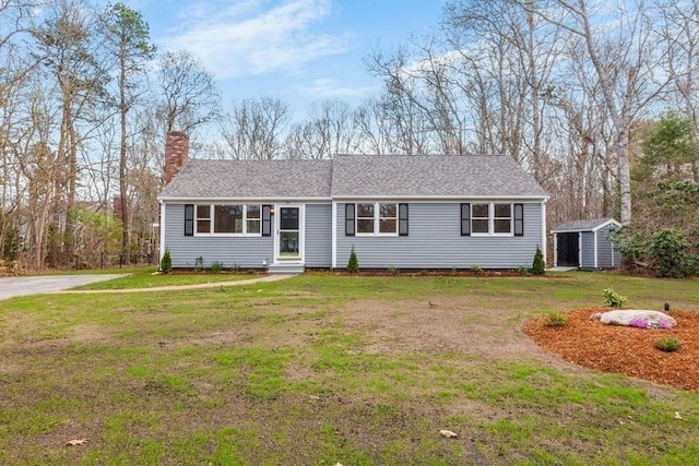 single story home featuring a shed, a front yard, entry steps, a chimney, and an outdoor structure