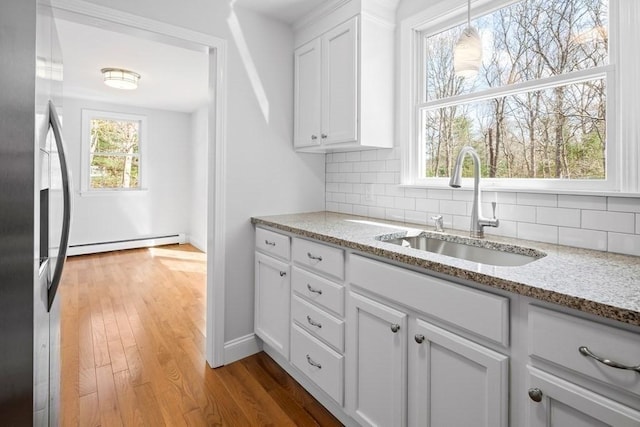 kitchen featuring decorative backsplash, a sink, stainless steel fridge with ice dispenser, a baseboard radiator, and white cabinets