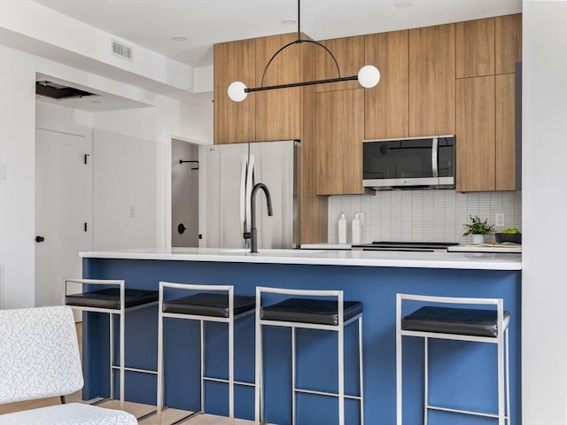 kitchen featuring stainless steel appliances, brown cabinets, visible vents, decorative backsplash, and light countertops