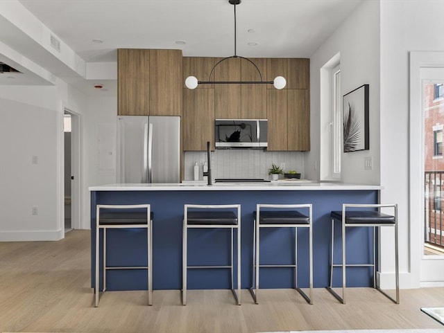 kitchen with light wood finished floors, brown cabinetry, modern cabinets, and appliances with stainless steel finishes