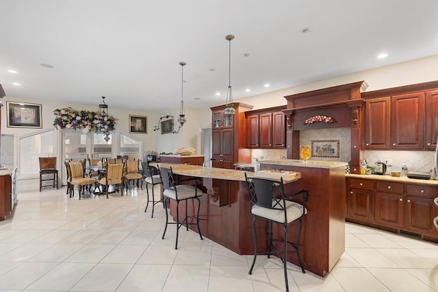 30 Bridle Path, Shrewsbury, MA 01545 - kitchen with an island with sink, light tile patterned floors, a kitchen bar, backsplash, and pendant lighting