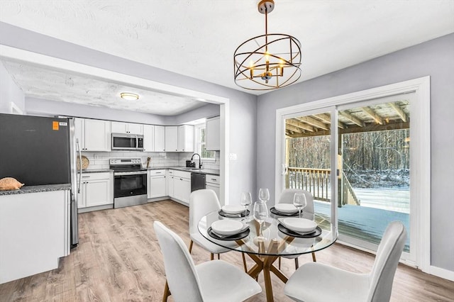 dining space with sink, light wood-type flooring, and a notable chandelier