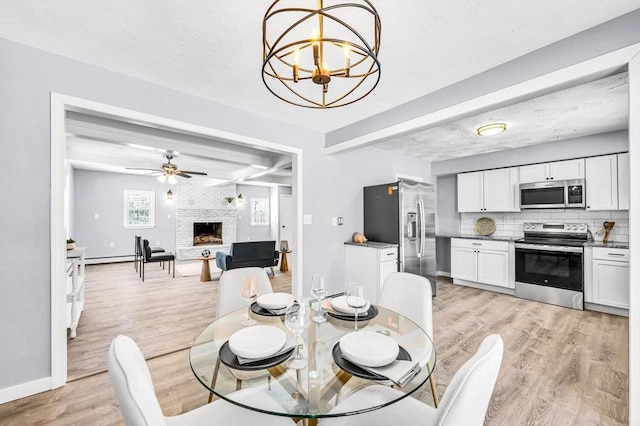 dining area featuring a baseboard heating unit, ceiling fan with notable chandelier, a brick fireplace, light wood-type flooring, and beam ceiling