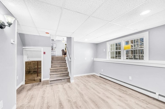 unfurnished living room with ceiling fan, light hardwood / wood-style flooring, a drop ceiling, and a baseboard heating unit