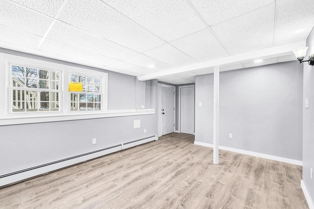 basement with light wood-type flooring, a drop ceiling, and baseboard heating