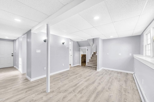 basement with baseboard heating, a paneled ceiling, and light hardwood / wood-style floors