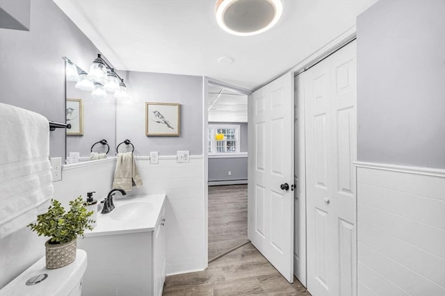 bathroom with a baseboard radiator, hardwood / wood-style floors, toilet, vanity, and tile walls