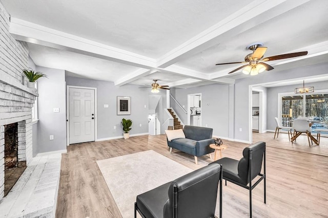 living room featuring ceiling fan, beamed ceiling, light wood-type flooring, and a brick fireplace