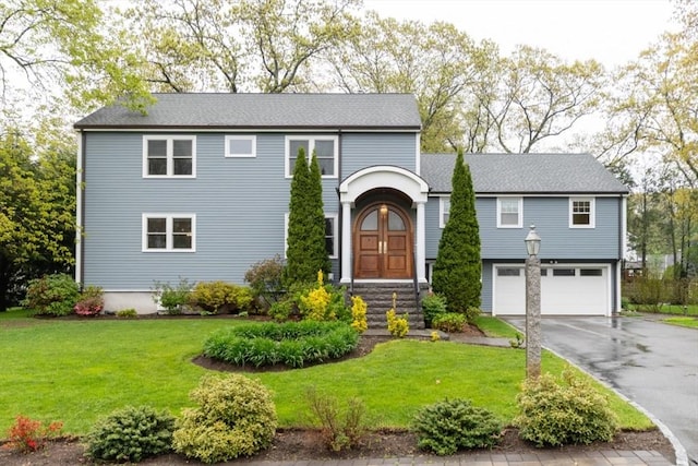 traditional-style home with an attached garage, driveway, a front yard, and roof with shingles