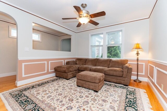 living area with wood finished floors, a wainscoted wall, ceiling fan, arched walkways, and a decorative wall
