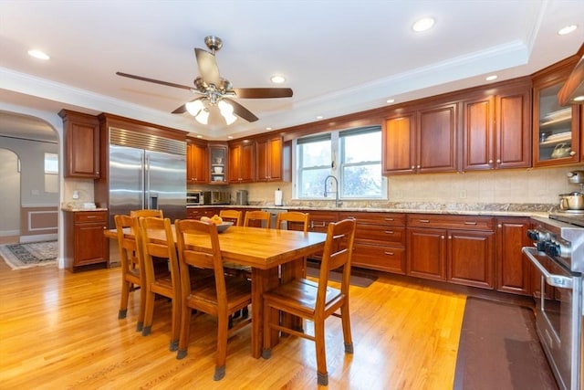 kitchen with premium appliances, arched walkways, light wood-style floors, ornamental molding, and glass insert cabinets