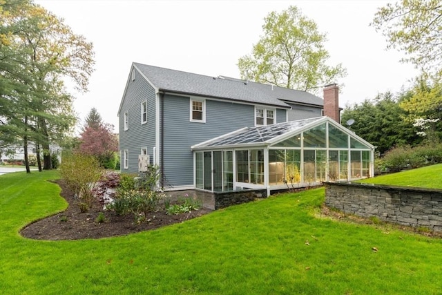 back of house with a sunroom, a chimney, and a lawn