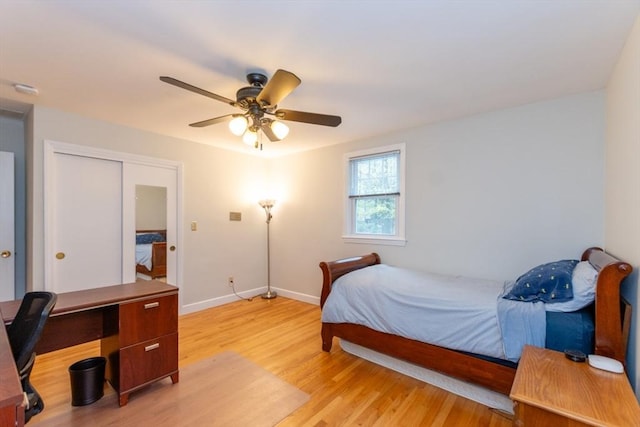 bedroom featuring light wood finished floors, baseboards, ceiling fan, a desk, and a closet