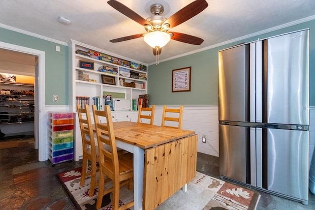 dining space with ornamental molding, a wainscoted wall, and a ceiling fan