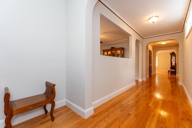 hallway featuring arched walkways, light wood finished floors, and baseboards