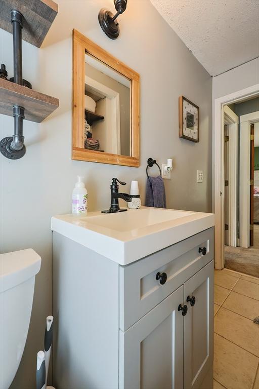half bath featuring toilet, tile patterned floors, a textured ceiling, and vanity