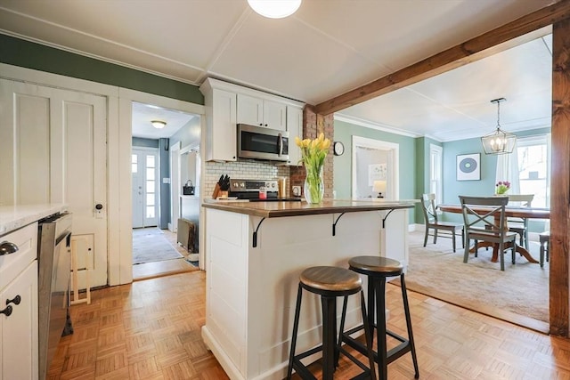 kitchen with appliances with stainless steel finishes, tasteful backsplash, ornamental molding, a breakfast bar, and white cabinetry