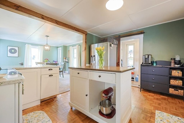 kitchen featuring stainless steel refrigerator with ice dispenser, pendant lighting, a center island, ornamental molding, and white cabinetry