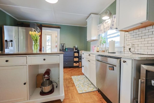 kitchen with crown molding, white cabinetry, a sink, backsplash, and stainless steel appliances