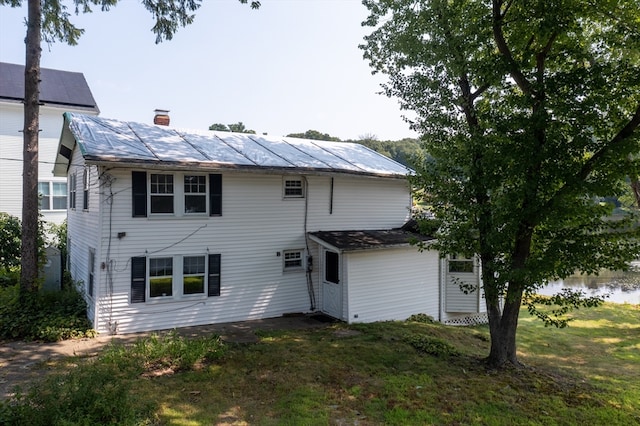 rear view of property featuring a yard and solar panels