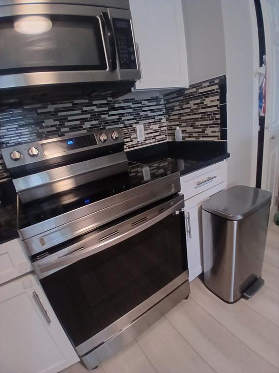 474 Revere Beach Blvd Unit 205, Revere, MA 02151 - kitchen featuring appliances with stainless steel finishes, decorative backsplash, white cabinetry, and dark countertops