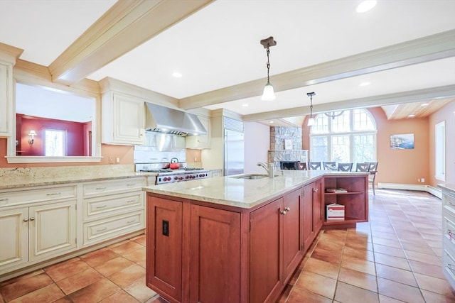 kitchen with wall chimney range hood, built in refrigerator, a sink, beam ceiling, and stove