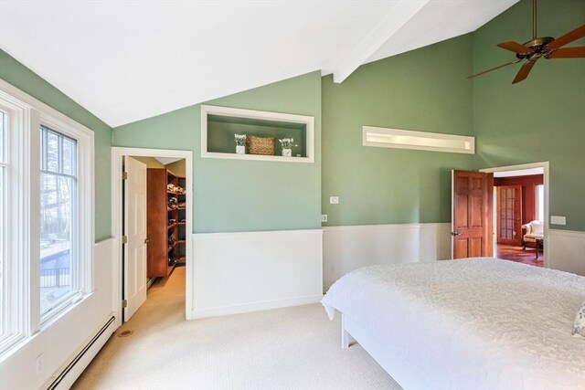 carpeted bedroom with lofted ceiling, a walk in closet, a baseboard radiator, and multiple windows
