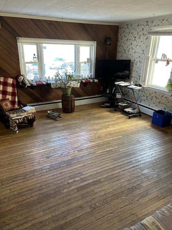 living area with a baseboard heating unit, plenty of natural light, and wood-type flooring