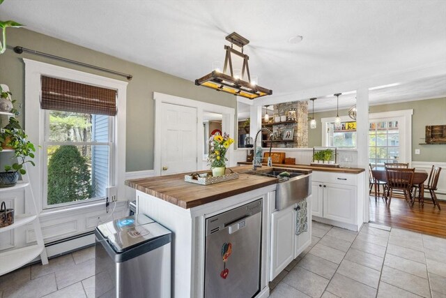 kitchen featuring a sink, dishwasher, wood counters, white cabinetry, and a center island with sink