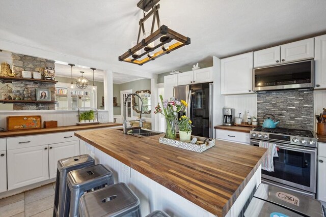 kitchen with wooden counters, appliances with stainless steel finishes, tasteful backsplash, a sink, and white cabinetry