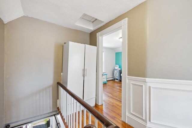hallway with an upstairs landing, wood finished floors, and a wainscoted wall