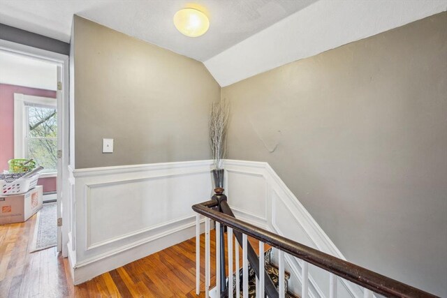 corridor with a wainscoted wall, a baseboard radiator, light wood-style flooring, and an upstairs landing
