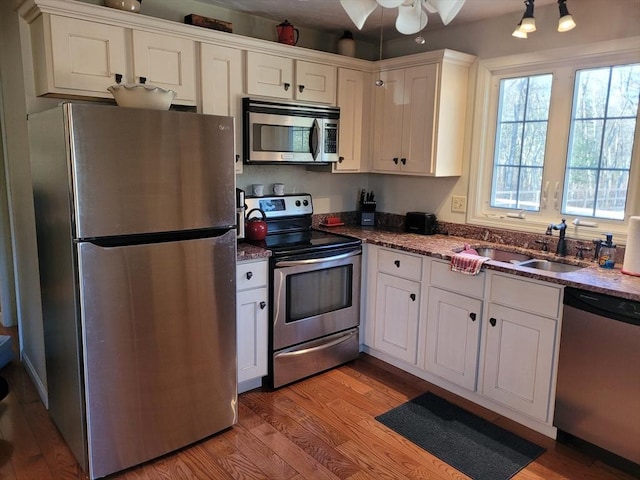 kitchen with sink, white cabinetry, dark stone countertops, stainless steel appliances, and light hardwood / wood-style floors