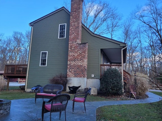 rear view of property with a wooden deck, a fire pit, a lawn, and a patio