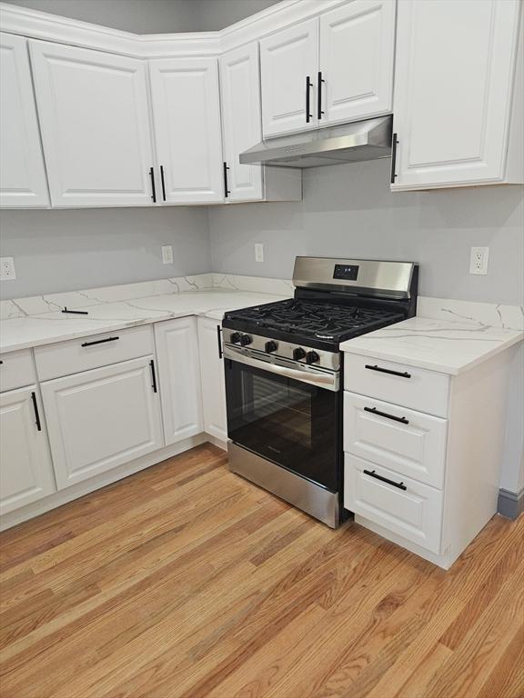kitchen with white cabinets, light wood finished floors, under cabinet range hood, and stainless steel range with gas cooktop